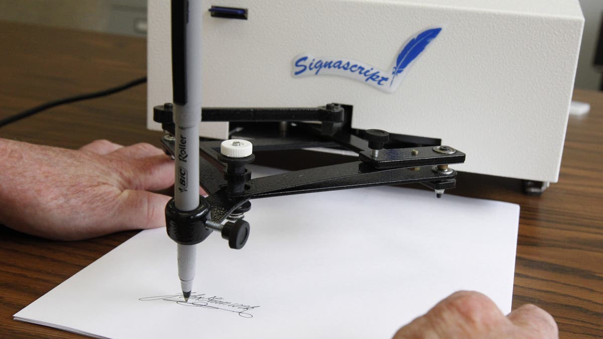 Damilic Corp. president Bob Olding anchors a sheet of paper as the Atlantic Plus, the Signascript tabletop model autopen, produces a signature at their Rockville, Md., office, June 13, 2011. (Manuel Balce Ceneta, File/The Associated Press)