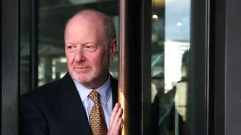 Photo by ANDY RAIN/EPA-EFE/REX/Shutterstock Former sub-postmaster Alan Bates in 2024 dressed in suit and tie going through a revolving door
