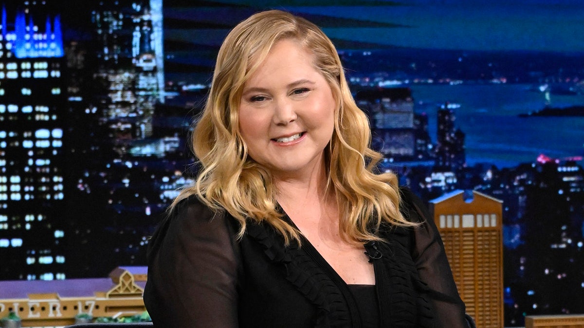Amy Schumer smiles wearing black dress