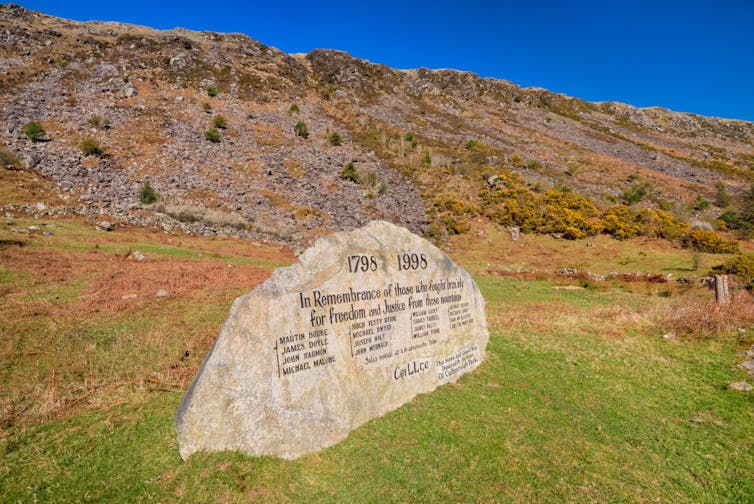 A large inscribed stone sits at the bottom of a hill with some vegetation.