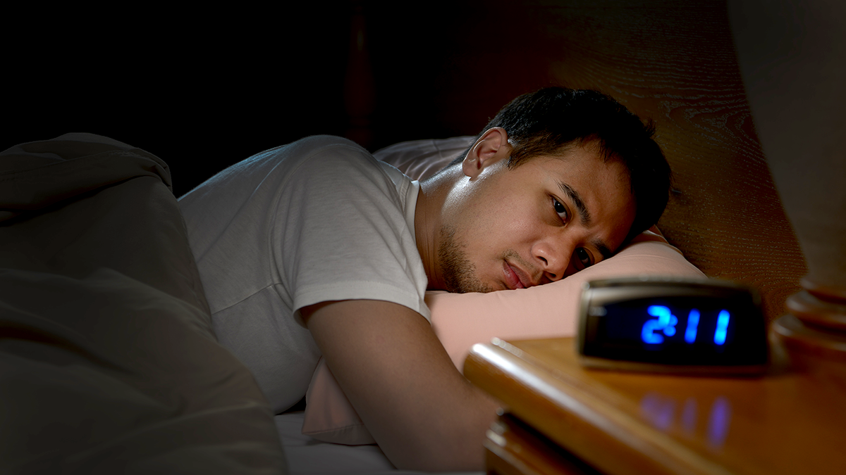 man lies awake in bed late at night