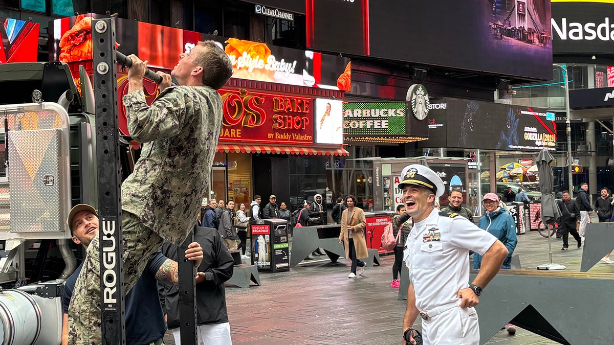 Military personnel at a Fleet Week event in Times Square (NYC). One does a chin-up while a crowd looks on.