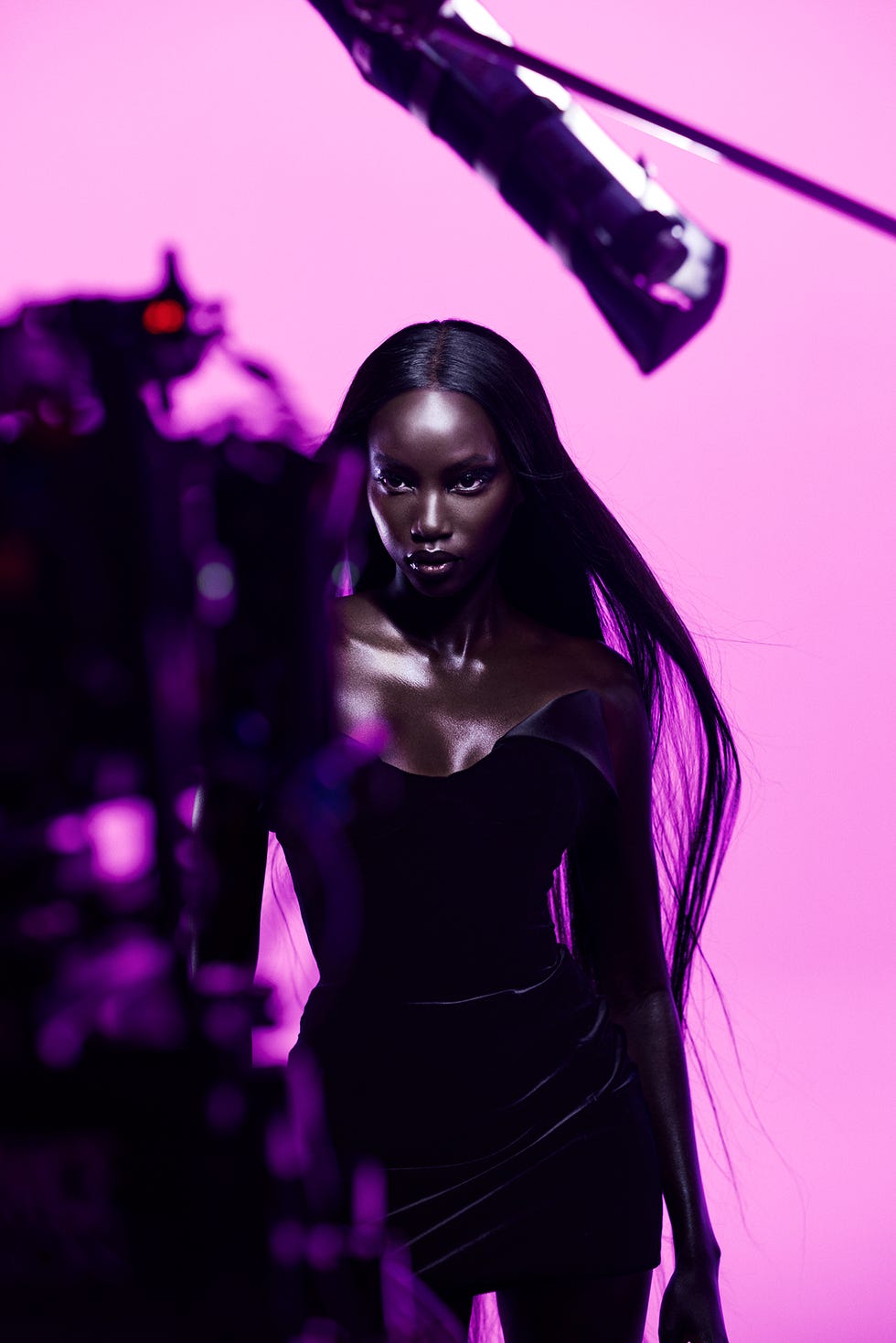 a model in a black dress is posed in front of a pink background
