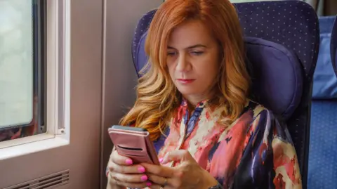 Getty Images Woman sitting on train looking at her phone