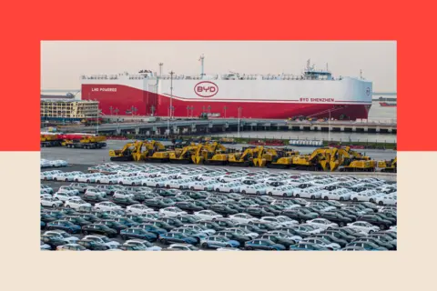 STR via Getty Lines of cars in a car park, in front of a BYD container ship