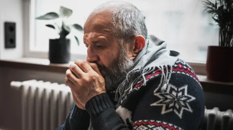 Getty Images A man in a Christmas jumper huddles for warmth next to a heater