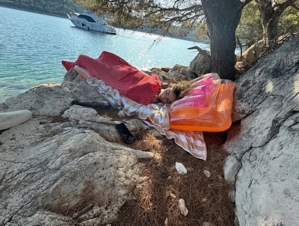 person resting on a rocky beach near water with floating lounge