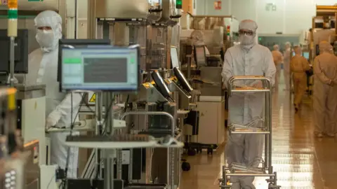 Getty Images Scientists in white protective clothing are seen working among computers and large machines.