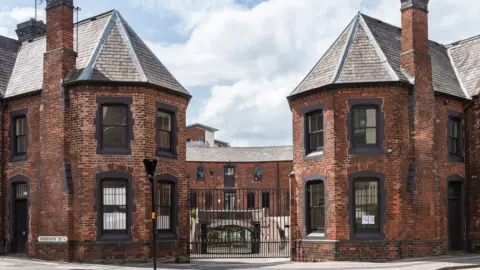 Roundhouse Birmingham A view of a horse-shoe shaped 18th century brick building with black framed windows and black iron gates at the front