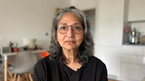 Fatima, a woman with shoulder-length greying hair, wearing glasses and a black top