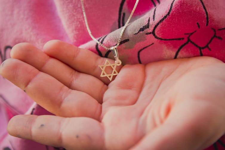 Someone wearing a pink shirt cups a small necklace with a six-pointed star in their hand.
