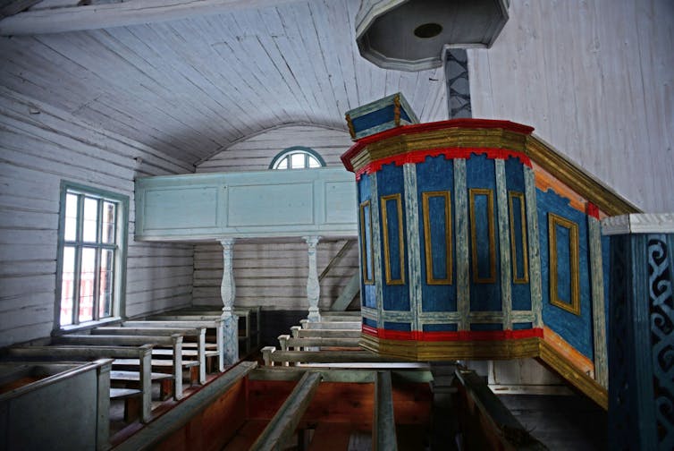 The sanctuary of an old church, painted in white and light blue, with a more brightly colored pulpit.