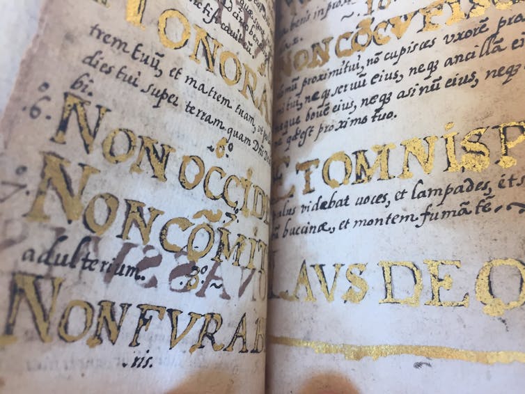 An open manuscript with large lettering in gold and black.
