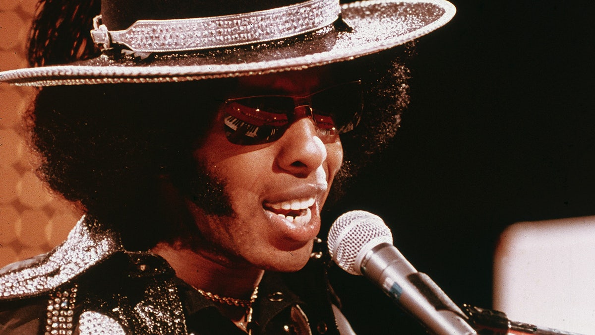 A close-up of Sly Stone singing to the mic.