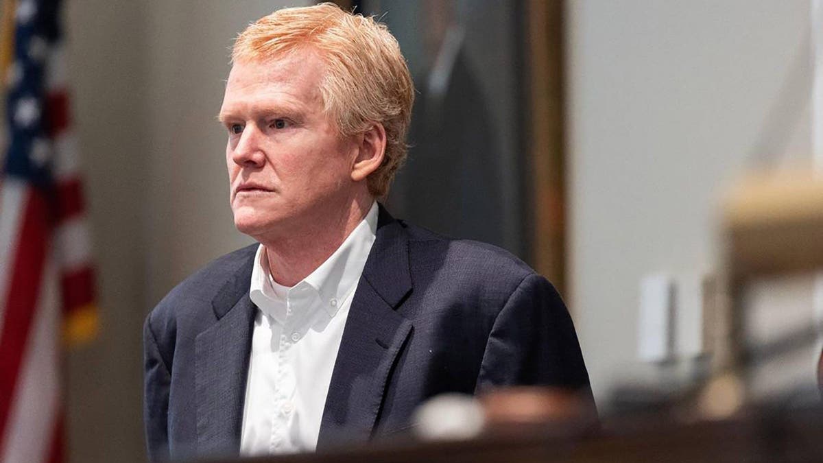 Alex Murdaugh stands in court, wearing a dark suit jacket, white shirt and no tie
