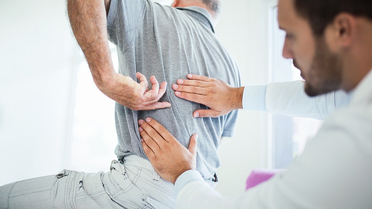 Spinal surgeon feels patient's back as he gestures to specific area.