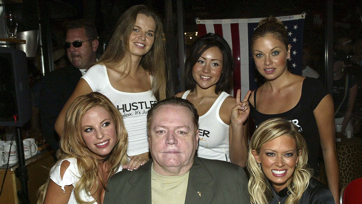 Larry Flynt surrounded by young women smiling.