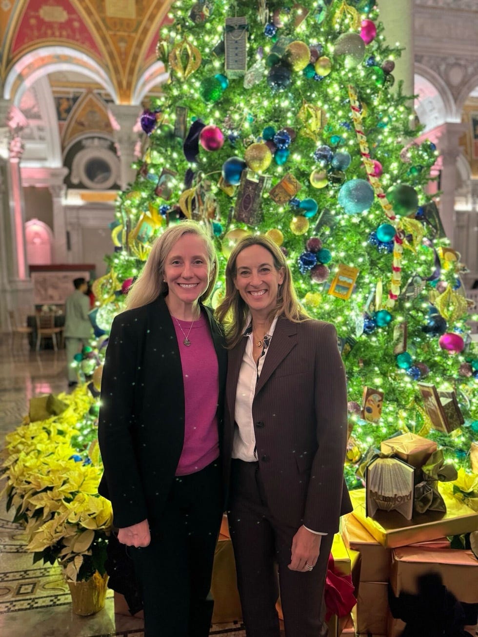 two individuals posing in front of a brightly decorated christmas tree