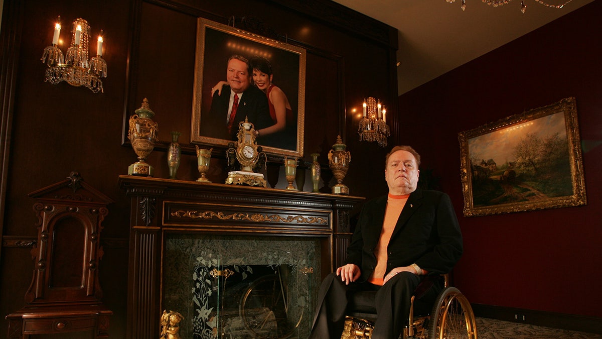 Larry Flynt sitting in a wheelchair next to a portrait of himself and his wife.