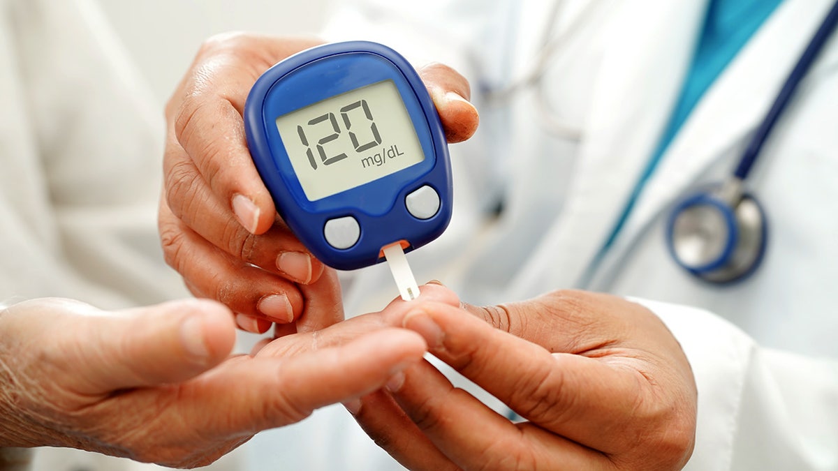 Asian doctor using digital glucose meter for check sample blood sugar level to treatment diabetes.