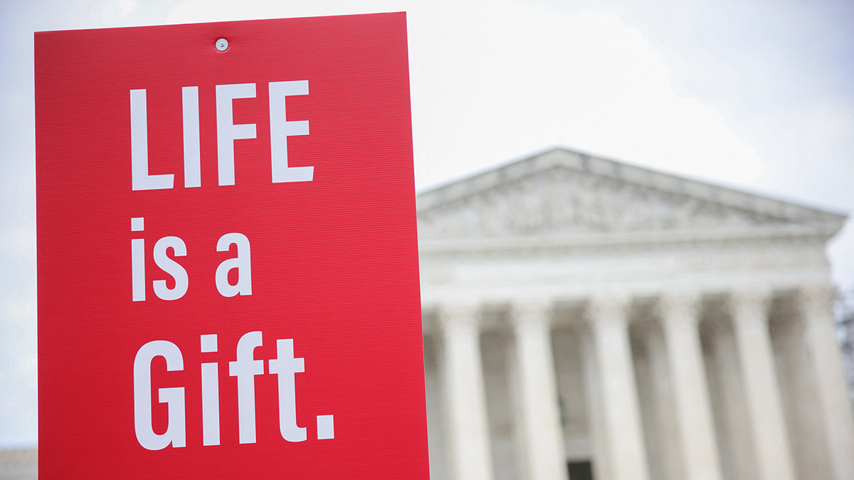 red sign in white letters; LIFE is a Gift; scotus building in background