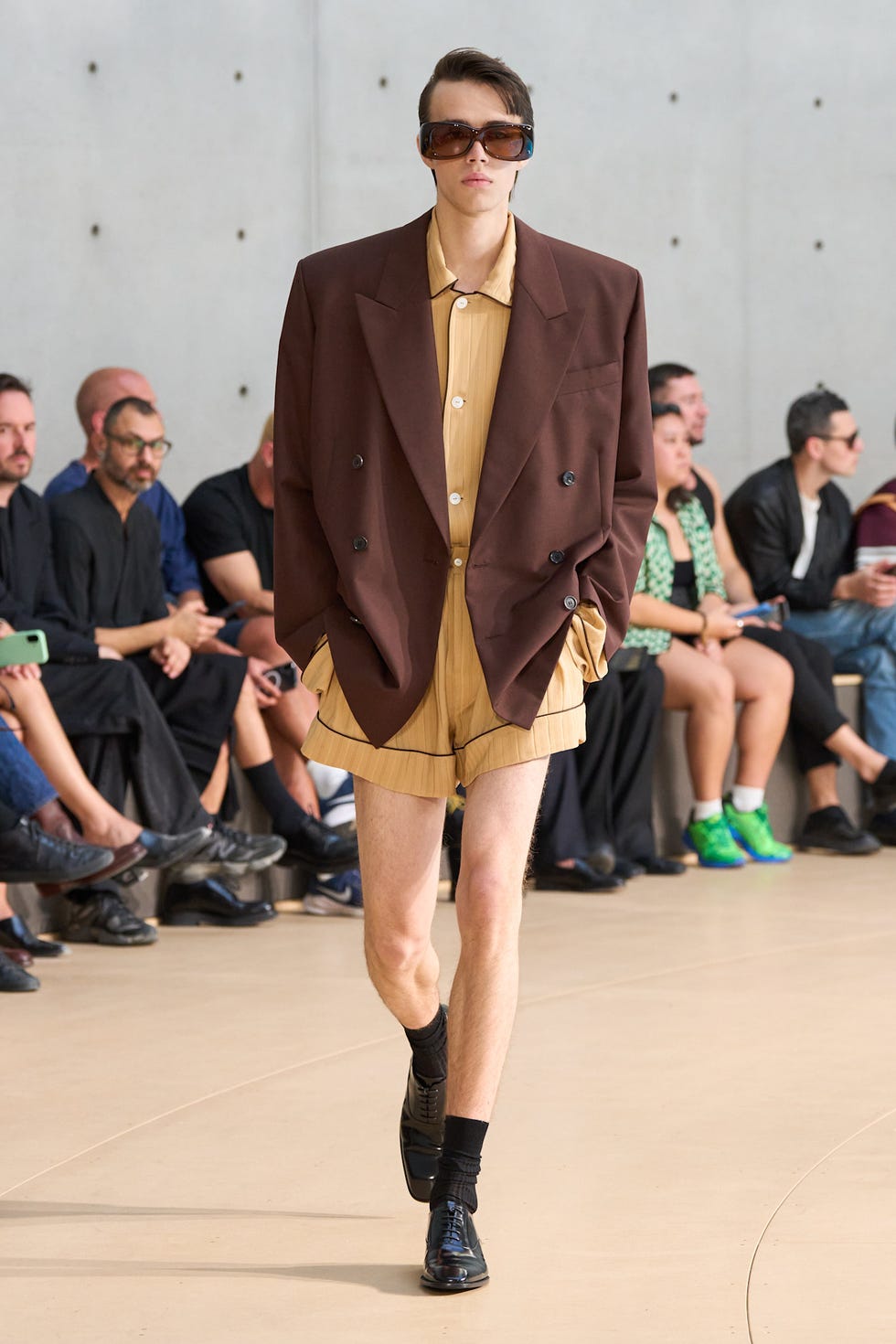 Fashion model showcasing a brown oversized blazer and beige shorts during a runway show