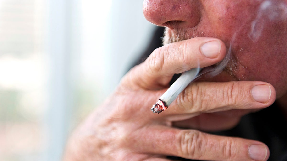 Older caucasian man zoomed in on with his fingers in focus as he smoked a cigarette