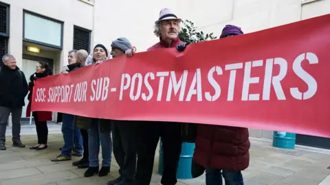 PA Media A group of people holding up a long red sign with the text: SOS support our sub-postmasters