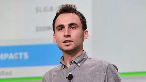 Getty Images Nikita Bier, wearing a grey, button-up shirt with a microphone attached, speaks on-stage at TechCrunch Disrupt in 2013.