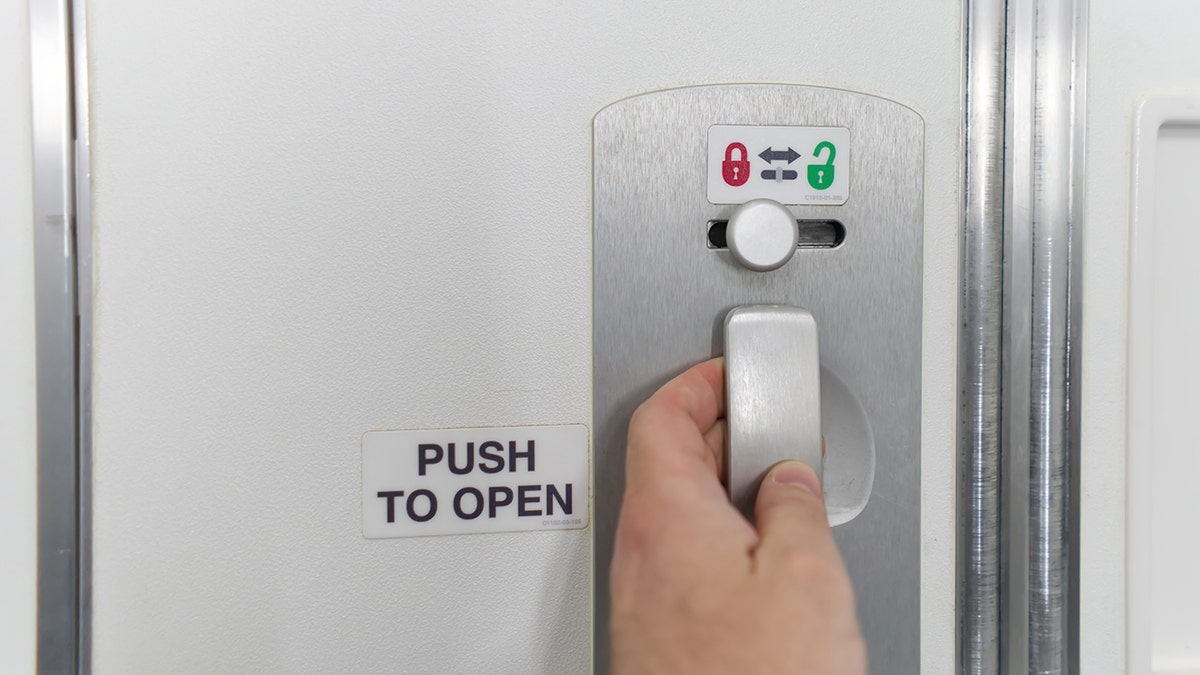 person grabs door handle to bathroom on plane