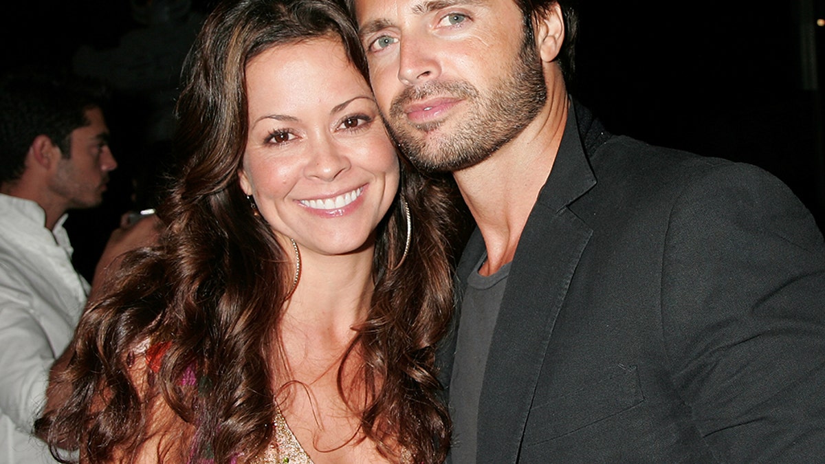 Brooke Burke and David Charvet posing and smiling together in front of a camera.