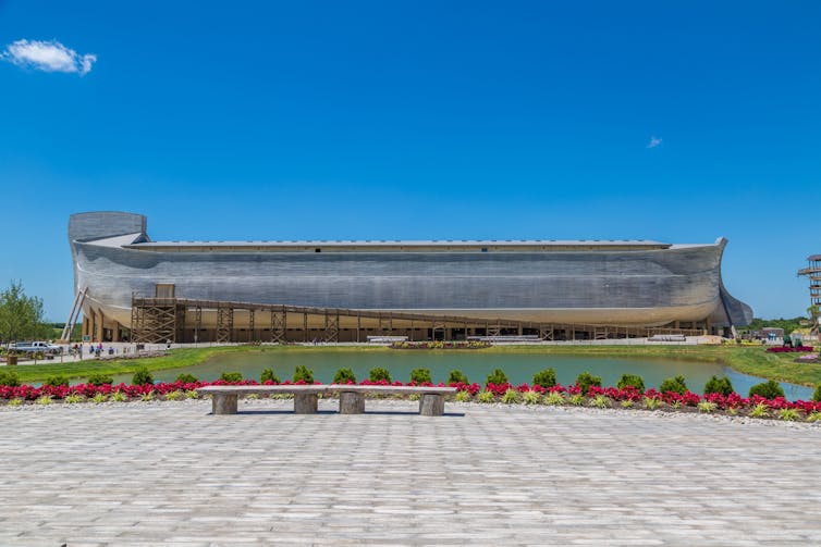 A large wooden ship resting on the ground with people walking nearby.