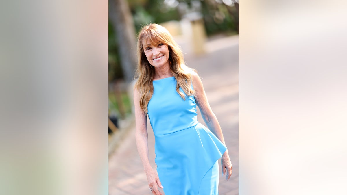 Jane Seymour wearing a blue sleeveless dress walking outside.