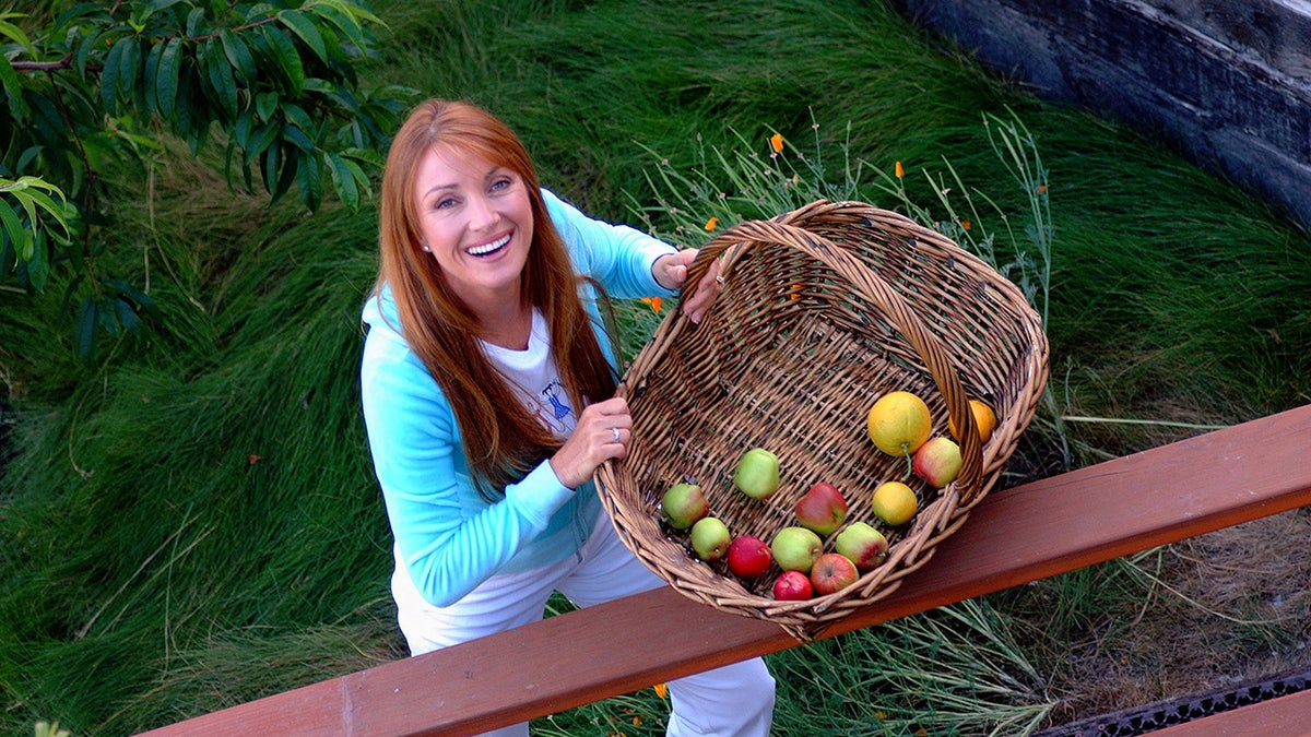 Jane Seymour looking up with a wicker basket holding apples.