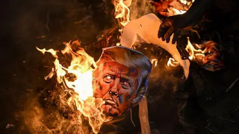 AFP via Getty Images A burnt effigy of US President Donald Trump seen with flaming embers. Activists from different unions were part of a protest against the tariff hikes imposed by the US on India during a demonstration in Kolkata on August 13, 2025. 