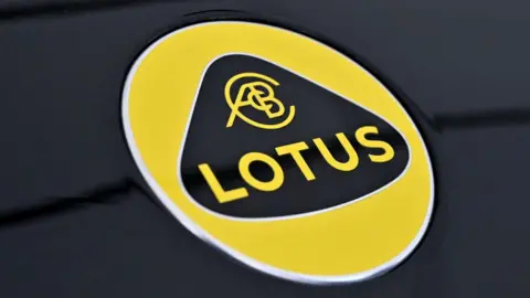 Getty Images The Lotus logo. It is a yellow circle which says LOTUS in yellow writing. The writing sits inside a curved triangle.