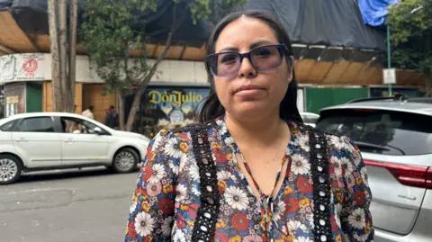 Erika Aguilar stands outside the apartment building where she and her family used to live on a street in central Mexico City