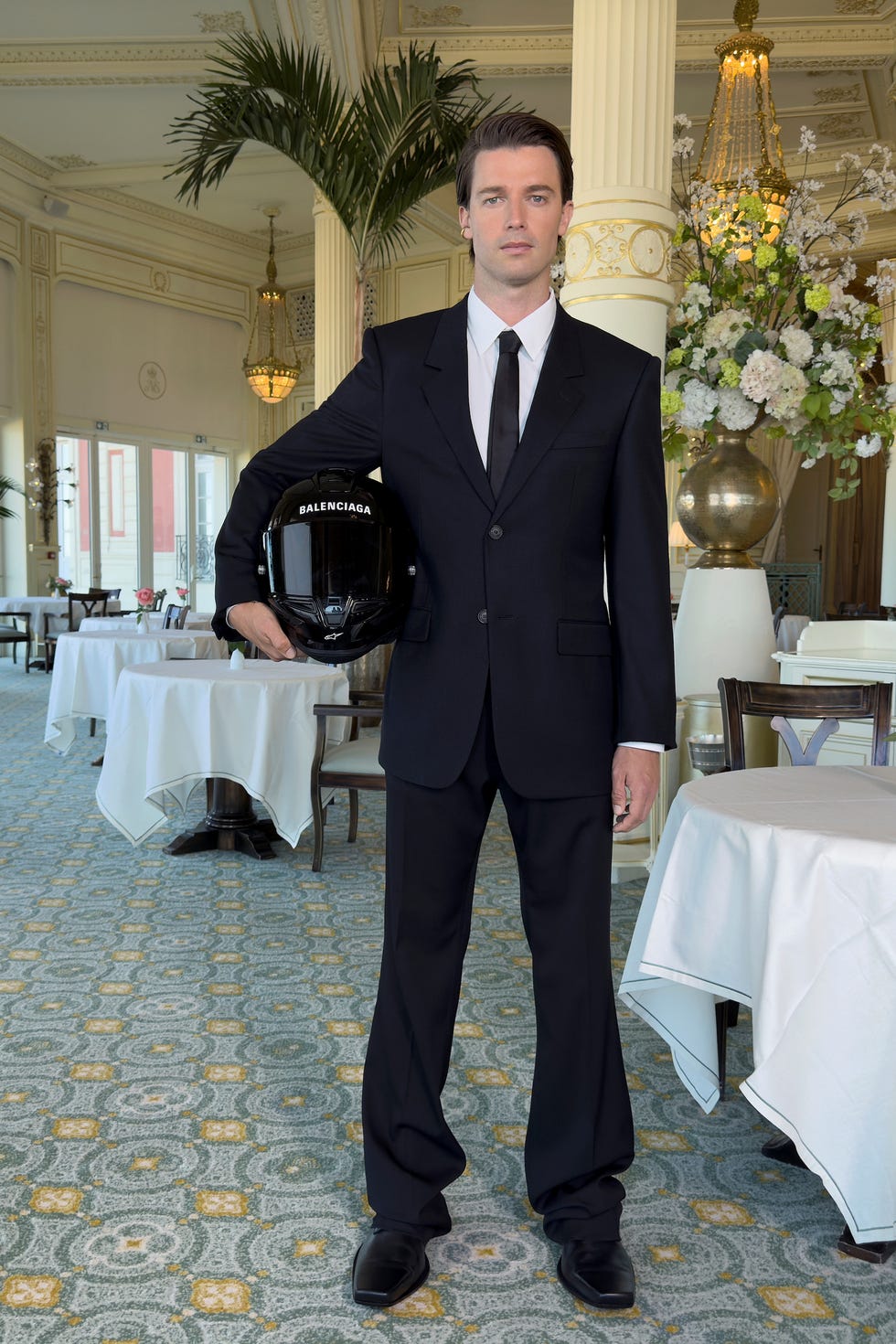 a man in a suit holding a helmet with a brand logo in an elegant dining environment