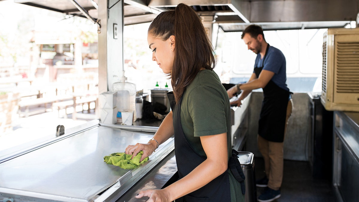 A man and woman clean a food truck.