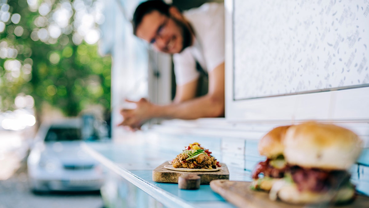 A wooden tray of tacos is in focus outside a food truck.