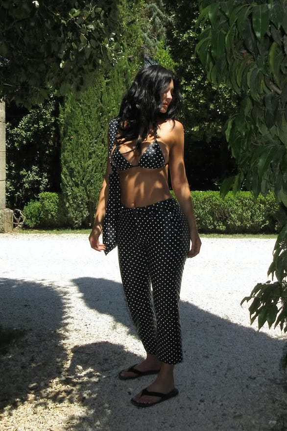 a person poses in a garden dressed in a polka dot bikini top and patterned pants