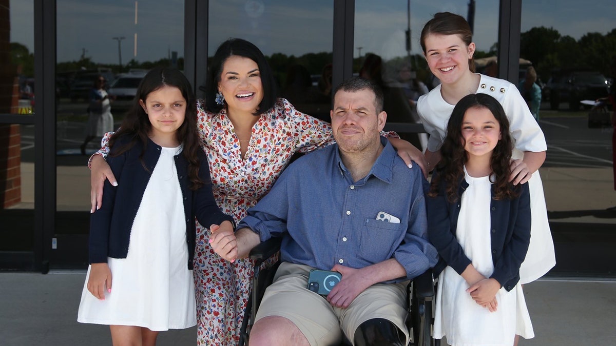 Michael Verardo with wife Sarah and their three daughters outside a building smiling together.