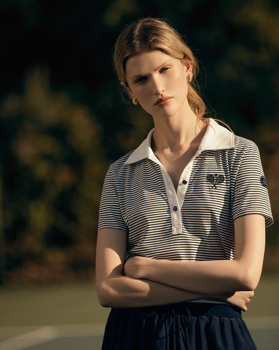 a person wearing a striped polo shirt and a dark skirt posing with arms crossed