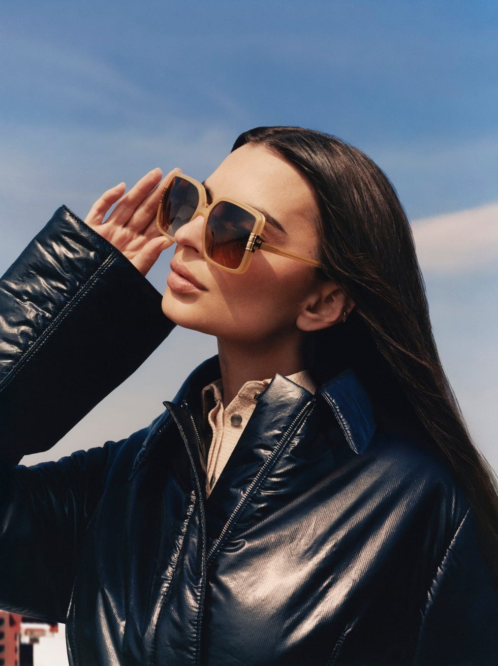 a woman wearing a stylish black jacket standing outdoors against a blue sky backdrop