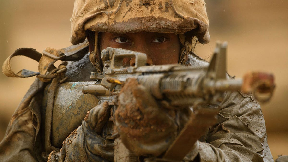 A female U.S. Marine Corps recruit aims her rifle while covered in mud following an obstacle course during training at Camp Pendleton, California, on April 21, 2021. (Patrick T. Fallon/AFP via Getty Images)