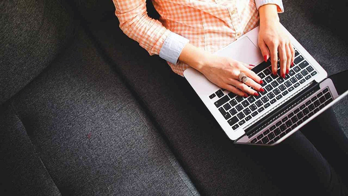 A woman with painted nails types on a MacBook.