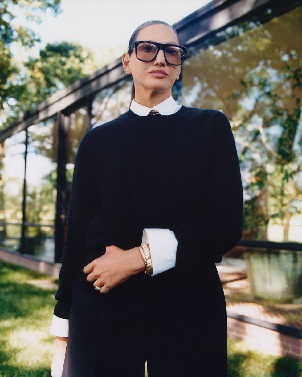a person dressed in a dark sweater and white collared shirt stands outside near a modern glass building