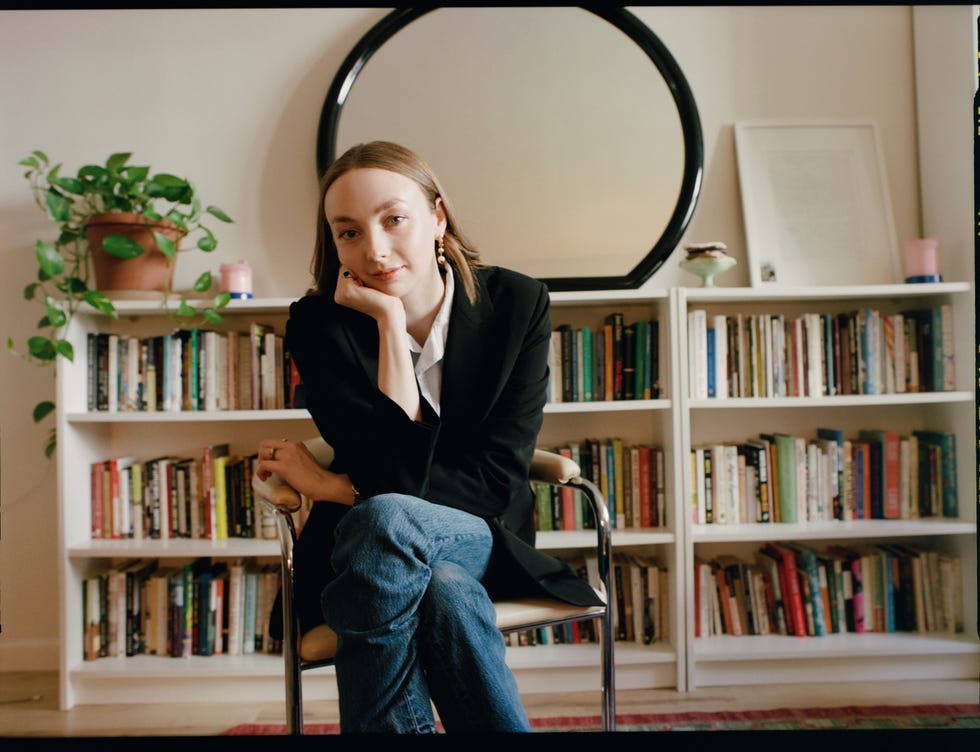 erika veurink seated in a modern interior environment with bookshelves and a plant