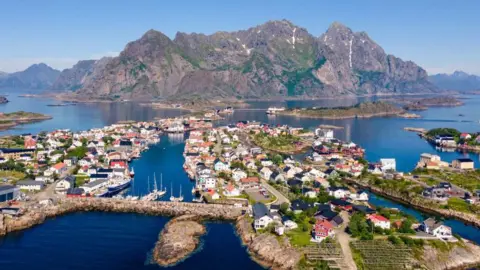 Getty Images Aerial view of the village of Hennigsvaer in northern Norway. Houses on islands are in the foreground with a large mountain in the background.