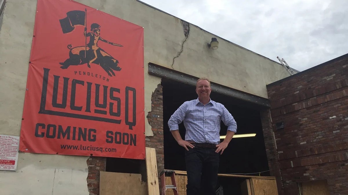 Lucius Q co-owner Aaron Sharpe standing outside building with "coming soon" sign for restaurant in 2017